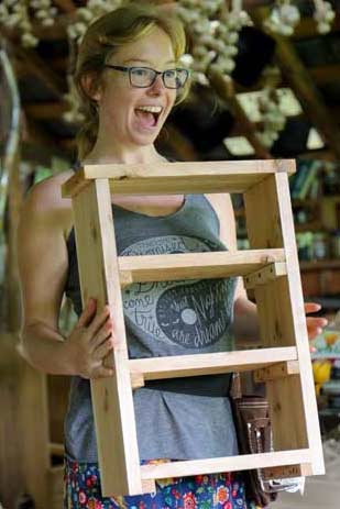 woman with a big smile holding a shelf that she built in a basic carpentry class