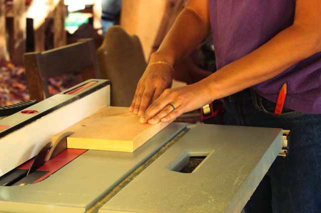 closeup of hands pushing a board through a table saw