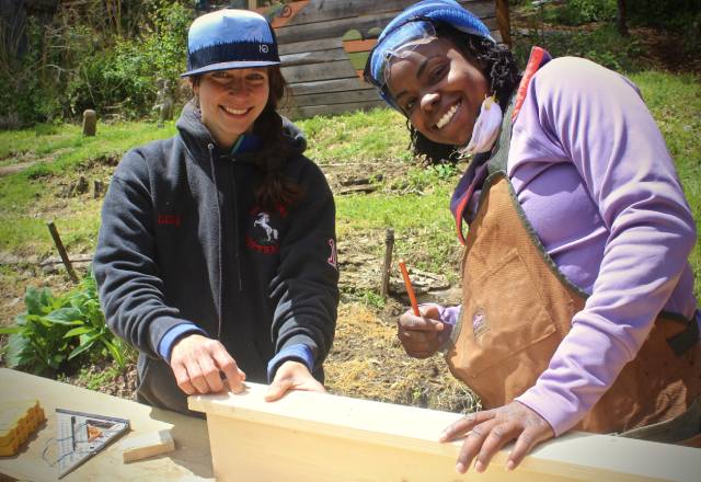 Ella Scotto and women's carpentry student measuring a board