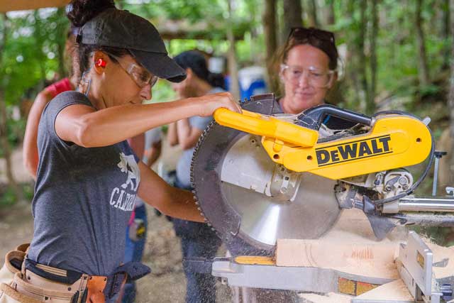 woman using a chop saw in a carpentry class