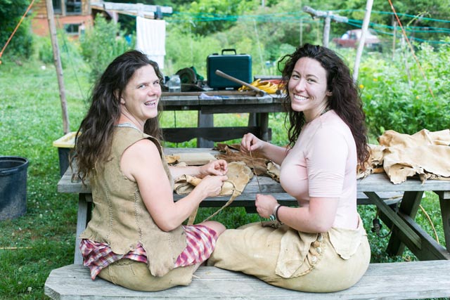 Two women sitting at a picnic table doing hand crafts