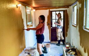 two women applying yellow DIY paint to drywall