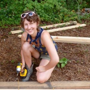 smiling female carpentry student Karen Shane with impact driver and lumber