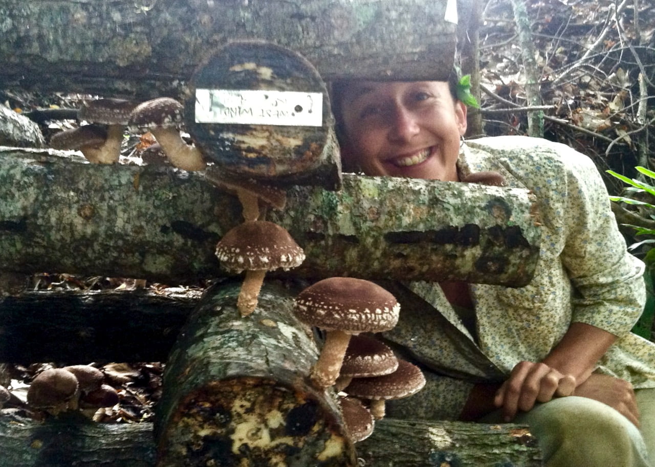 woman smiling with homegrown shiitake mushrooms on inoculated logs