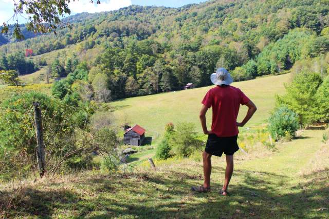 man from the back looking down at barn and field and mountains