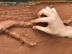 closeup of hand shaping cob in a natural building and permaculture design course