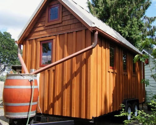 a tiny house with gutters and a rainwater catchment system including a rain barrel