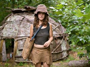 Natalie Bogwalker at the Wild Roots Community in front of a tulip poplar bark hut