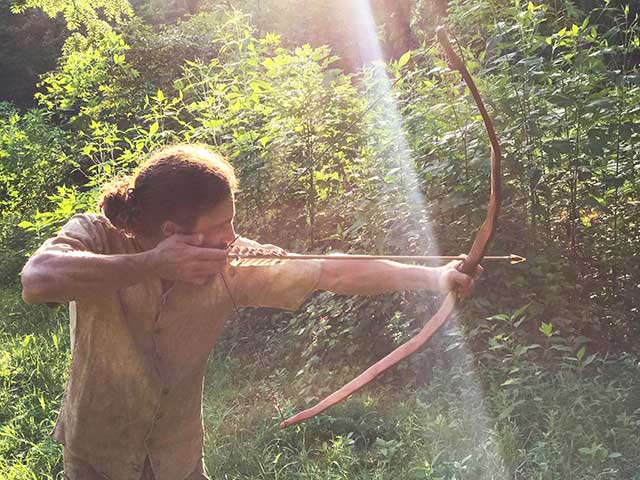 survival skills instructor Tyler Lavanburg shooting a bow and arrow wearing a buckskin vest