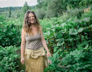 Natalie Bogwalker laughing in her garden next to okra plants