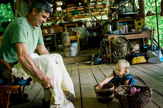 man stretching a deer hide during brain tanning with a little girl playing with a basket