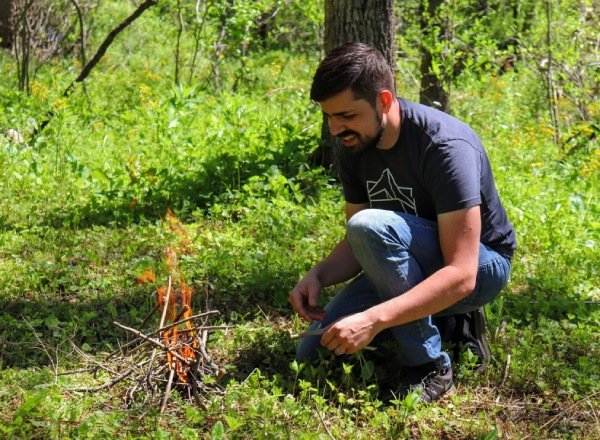 man building and tending to fire in the woods