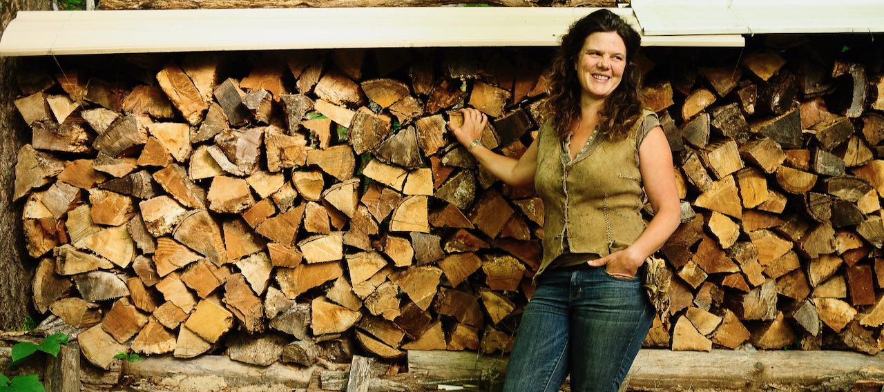Natalie Bogwalker standing in front of a firewood stack at Wild Abundance