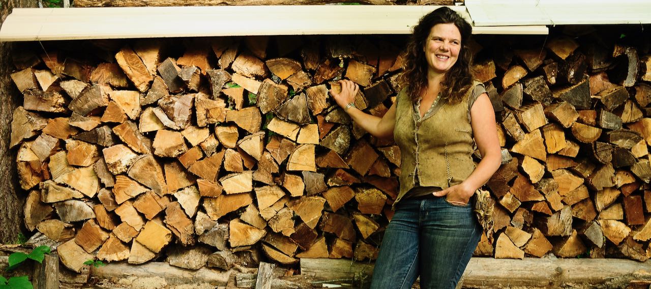 Natalie Bogwalker standing in front of a firewood stack at Wild Abundance