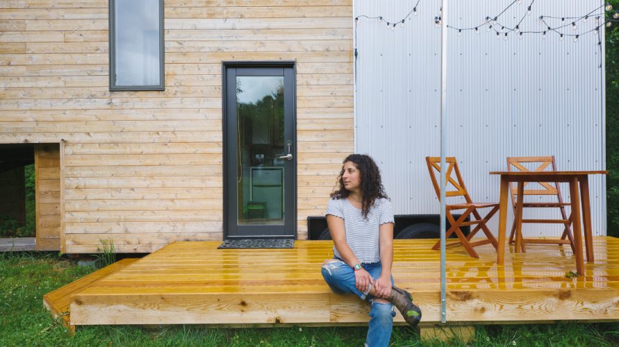 woman sitting on deck in front of tiny house on wheels