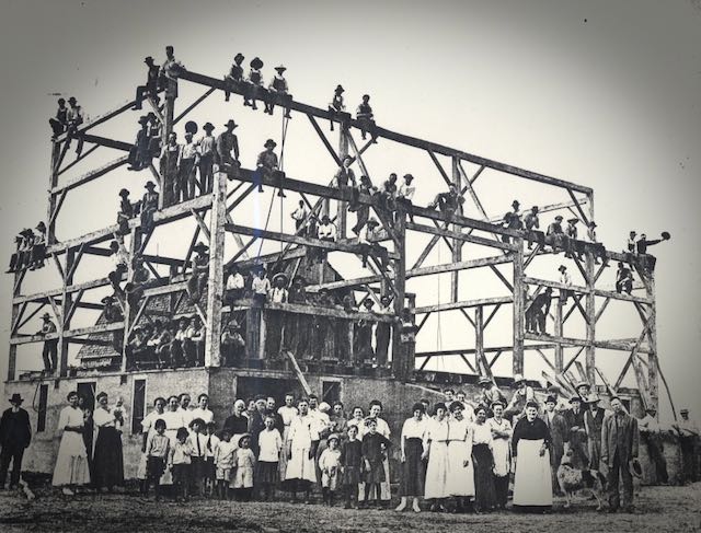Black and white photo of a large timber frame with people on it