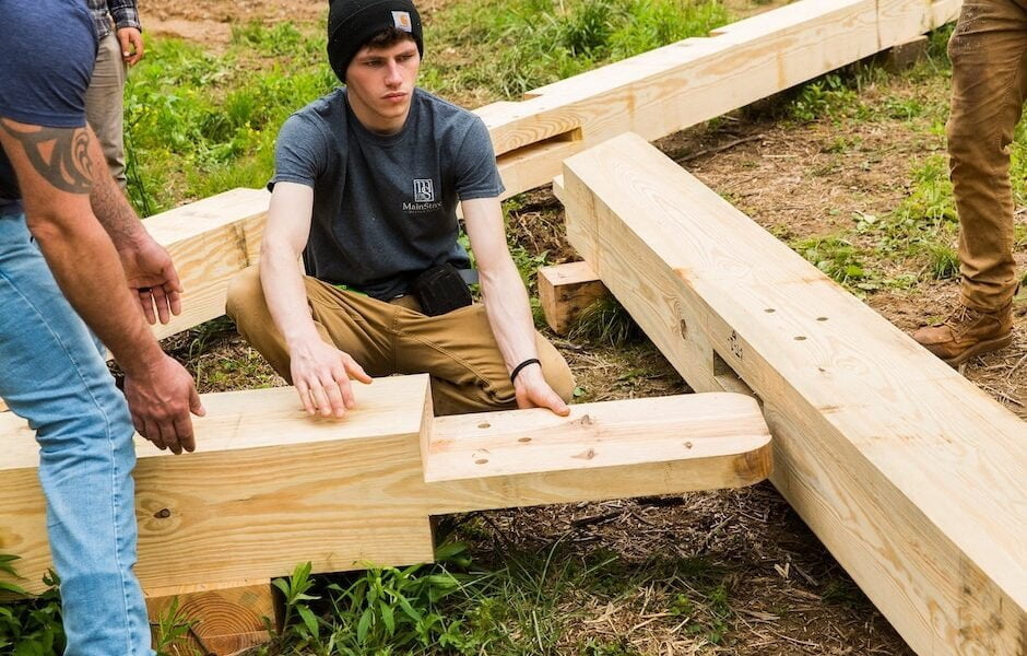 A student works on a timber frame bent framing on the ground during a building workshop