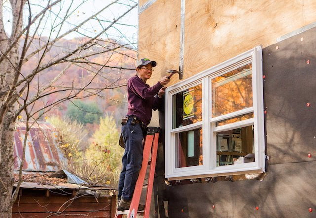 Student on ladder installing windows during tiny house class