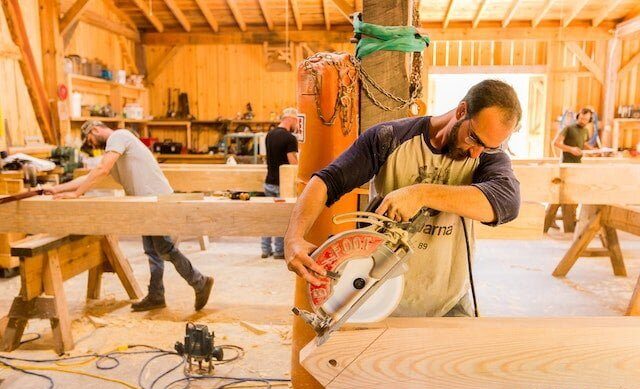 A male student uses a saw after mearsuring where to cut in a Timber Frame workshop