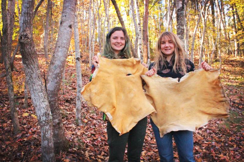 tow young women holding up buckskin they made with brain tanning