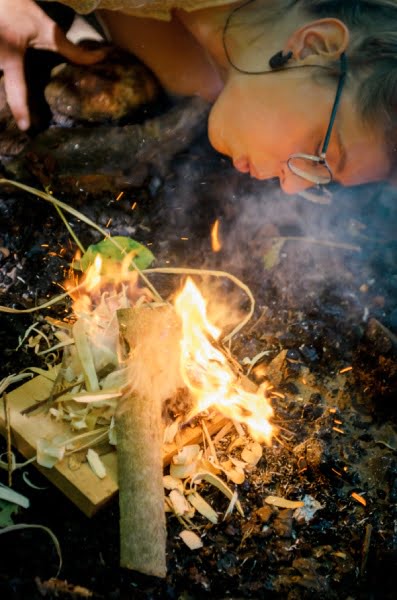 woman blowing on a fire during a survival campout