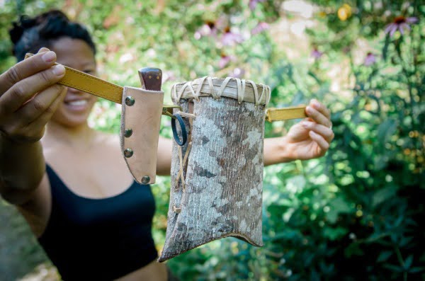 woman holding up a belt with a knife sheath, knife, and tulip poplar bark basket attached to it