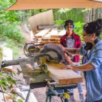 Women's Basic Carpentry students use table saw during class to cut thick wood