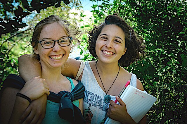 Two permaculture apprenticeship students smile and hug 