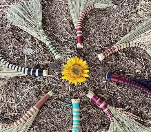 Brooms made during rewilding class lined up in a circle around a flower