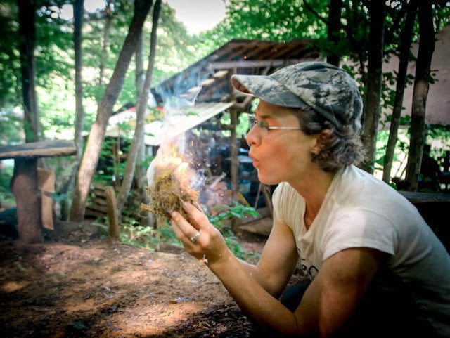 Woman blows on tinder to make a fire during rewilding class