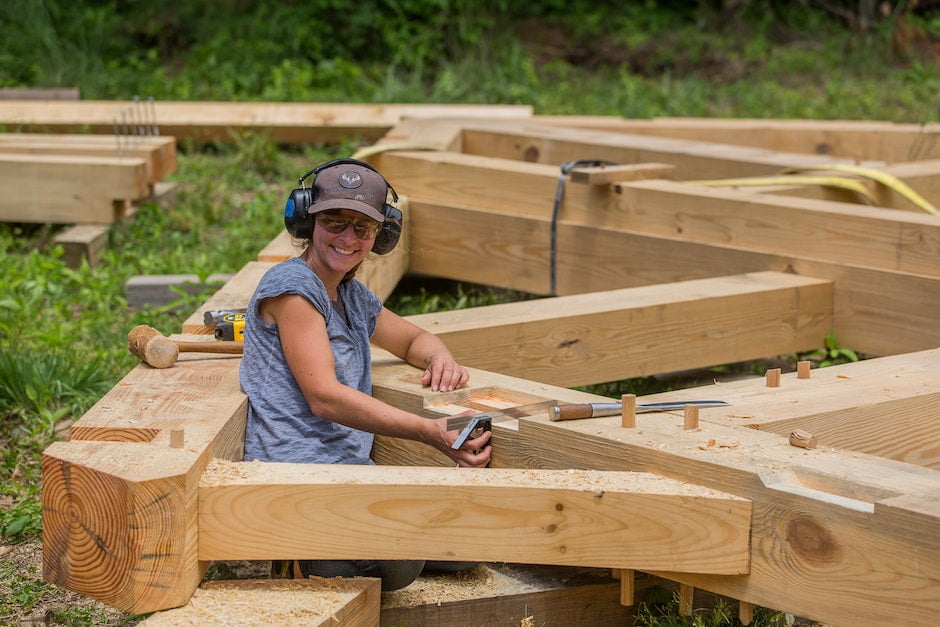 A female student smiles up from her work on preparing timber frame joinery