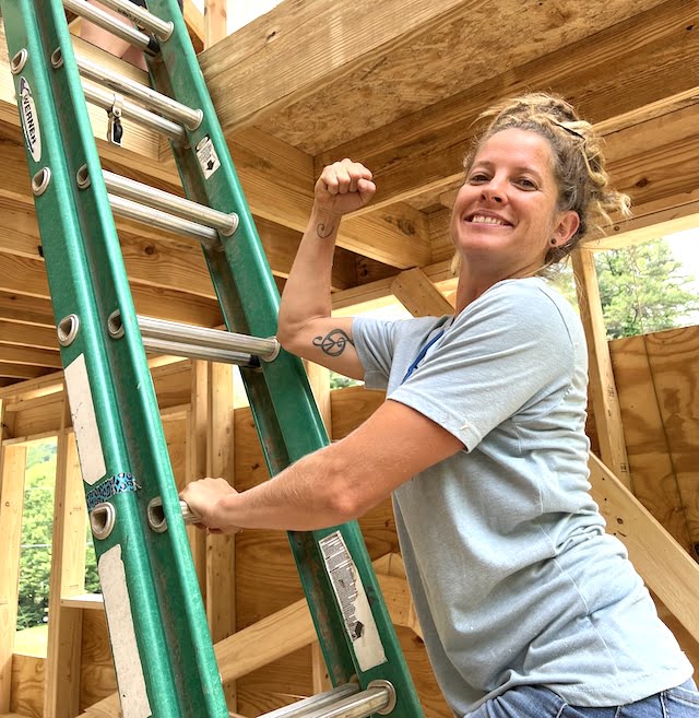 Student shows strong arm while posing on ladder during tiny house workshop