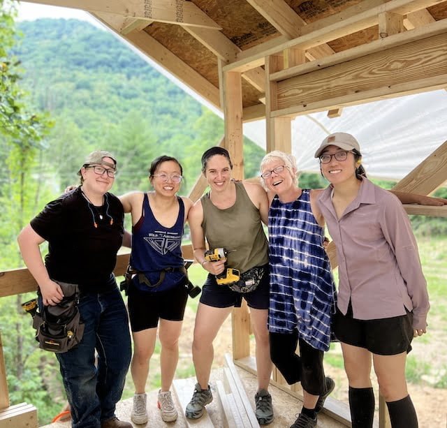5 students with their arms around each other pose in tiny house during workshop