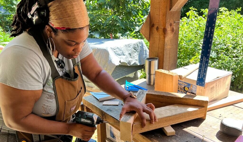 A women's carpentry student uses a drill to screw wood together