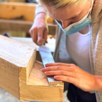 Woman wearing mask uses chisel during timber framing class
