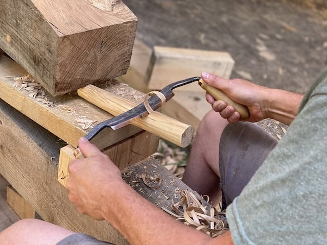closeup of hands using a draw knife and a shaving horse during Timber framing class