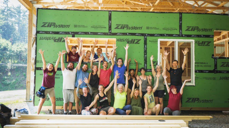 excited tiny house building students in front of a house with their hands in the air