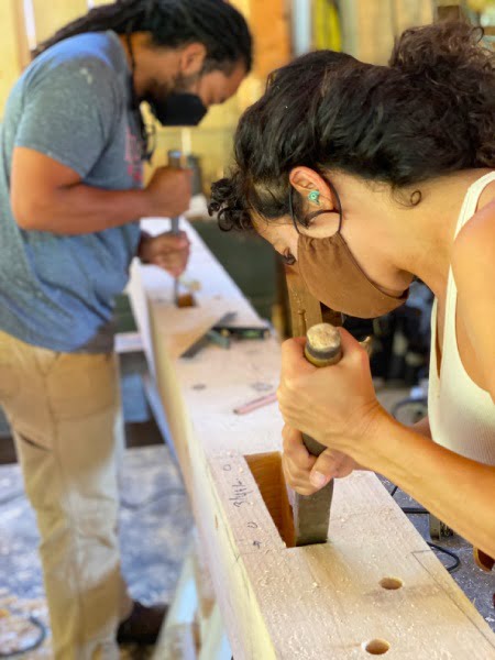 Two students with mask on use chisels during timber framing class