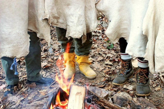 Feet of people drying hides around the fire during a hide tanning class