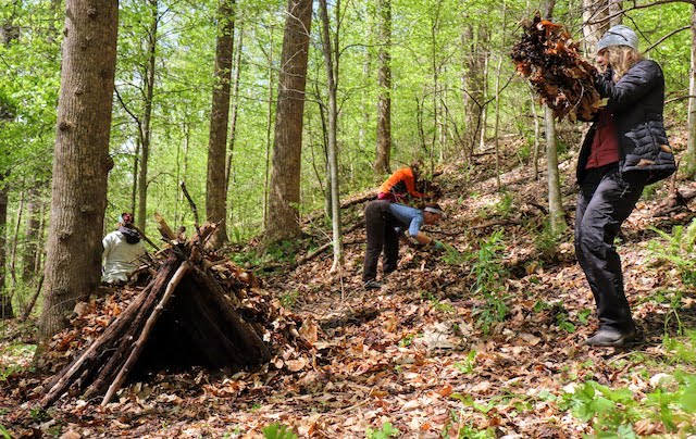 Four people building a debris shelter in the woods during a survival skills class
