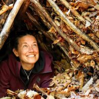 Student peeks out of shelter built in the woods during survival skills class