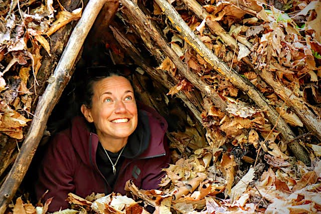 Woman smiles from inside a debris shelter during a survival class