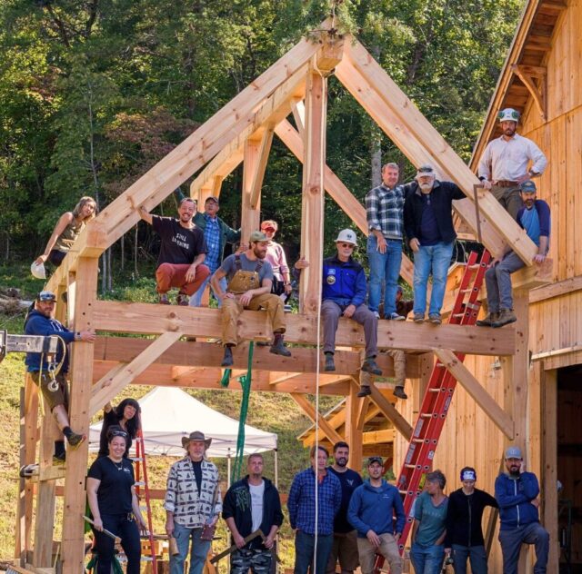 A group photo of a timber framing class with students posed on and in front of the structure they built during a workshop at Wild Abundance