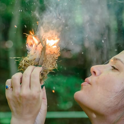 A woman blows on the flames in a clump of tinder as she learns to a fire during a survival skills class at Wild Abundance in North Carolina