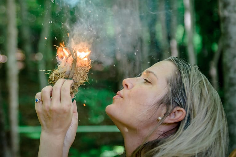 A woman blows on the flames in a clump of tinder as she learns to a fire during a survival skills class at Wild Abundance in North Carolina