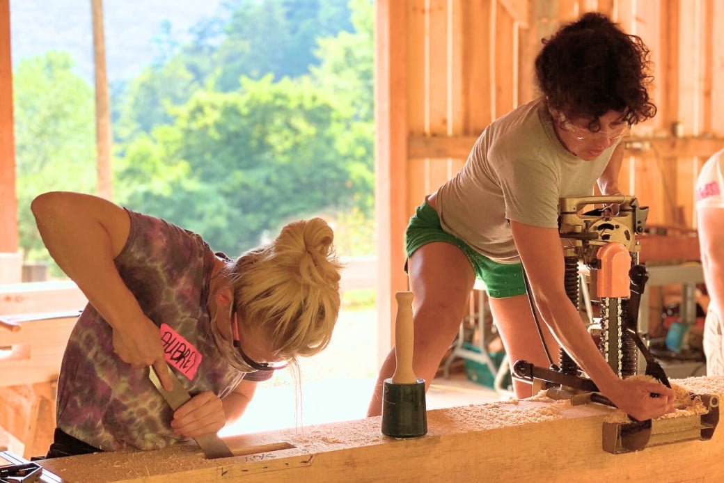 two female students using tools in a timber framing workshop