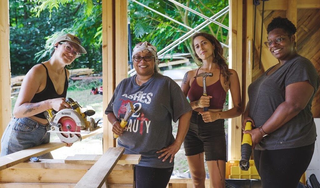 Four women stand holding tools during tiny house class