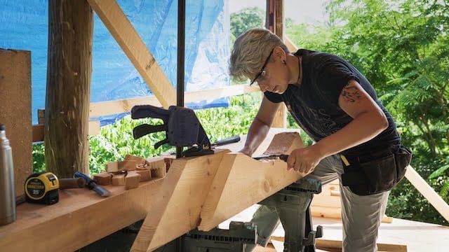 person using a draw knife to create a curve in a brace for a tiny house