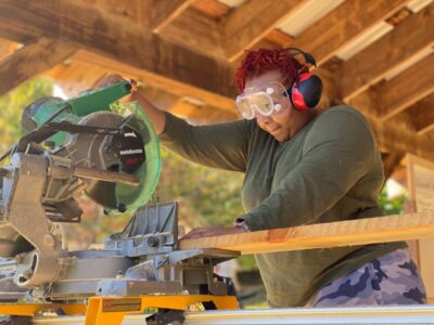 woman using a chop saw to build a tiny house