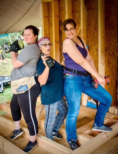 three women wielding tools to build a tiny house